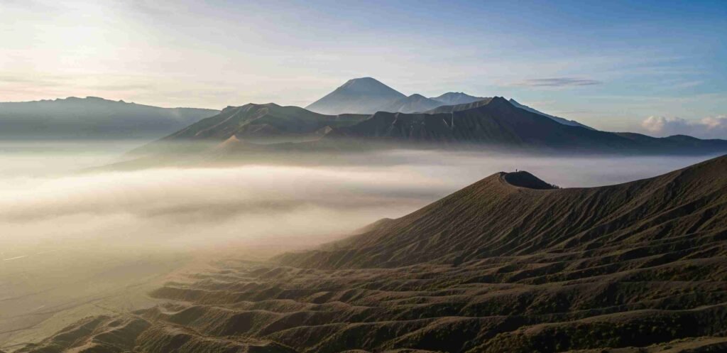 Pemandangan luas Pasir Berbisik di Taman Nasional Bromo Tengger Semeru, Indonesia, dengan kabut tipis yang menyelimuti hamparan pasir vulkanik yang luas. Pemandangan ini adalah daya tarik unik bagi mereka yang wisata ke Bromo.